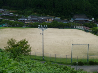 山や市街地に囲まれた土のグラウンドの写真