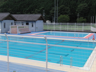 民家に隣接した、フェンスに囲まれた幼児用プールがある屋外プールの写真