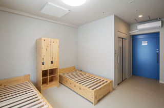 箪笥を挟んで布団が敷かれていない木製のベッドが2つ置かれている写真