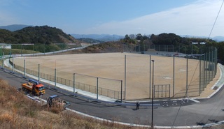 周囲が道路に囲まれた土の屋外グラウンドの写真