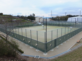 歩行者用通路とフェンスに囲まれた夜間照明施設のあるテニスコートの写真