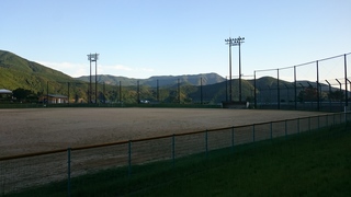山々や防護ネットに囲われたグラウンドの写真