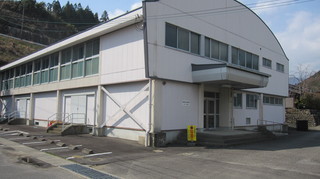 アスファルトの地面に囲まれた白い壁で奥行きのある建物の写真