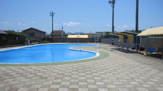 タイル張りのプールサイドに日よけと椅子が置かれている写真