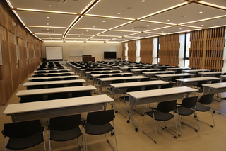 椅子と長机が4列に並べられている広い室内の写真