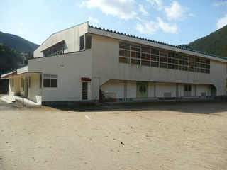 遠くに山が見える白い壁の奥行きのある2階建て建物の写真