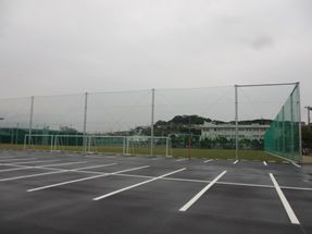 防護ネットに囲まれて複数サッカーゴールが置かれている芝生のグラウンドと駐車場が隣接している写真