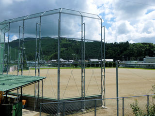 遠くに山が見える屋外の防護フェンスが敷かれたグラウンドの写真