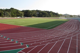 青空の下遠くに林が見える陸上競技用のトラックの写真