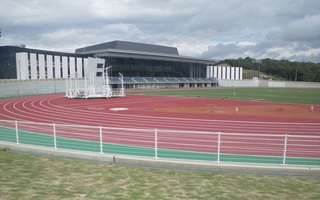 横に長い大きな建物の前にある陸上競技用の屋外トラックの写真