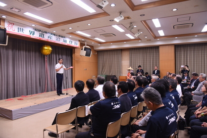 壇上で金色のくす玉を背にした男性がマイクを持ち話している写真