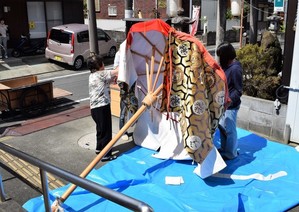 赤や金色の布でできた大きな笠の形に似たお祭りの道具を準備する2人の女性の写真