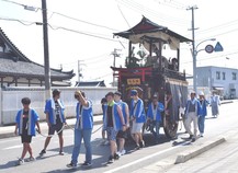 青い法被を着た人たちが山車を引いて歩いている写真