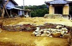 瓦屋根の小屋の前に土の上に石が積まれて置かれている写真