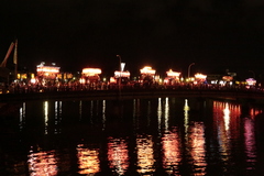 明かりがついた複数の山車が夜の橋を渡っている写真