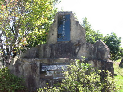 木々の中に建つ、下部に説明文が付いた大きな石碑の写真