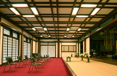 右側に畳、左側はカーペットにパイプ椅子が2列並ぶ和風の室内の写真