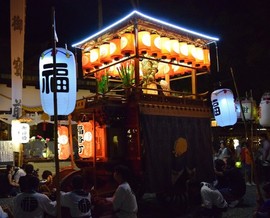 夜の中を進んでいる明かりがついた山車の写真