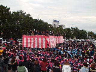 会場の中央でやぐらの上から餅まきが行われている全体の写真