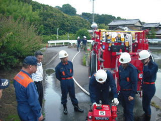 消防車の横で制服を着た団員たちが可搬ポンプの点検をしている写真