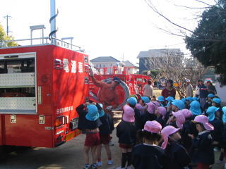 園庭で園児たちが消防車の前に集まって見学している写真