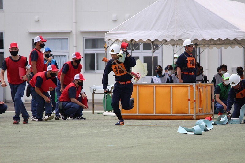 運動場で制服を着た団員が資機材を抱えて走っている写真