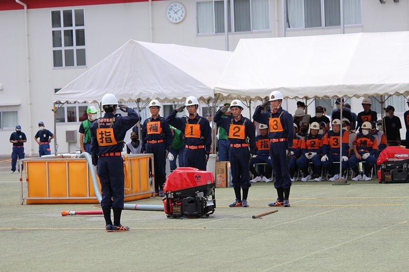 運動場のテント前で制服を着た団員たちが整列して敬礼している写真