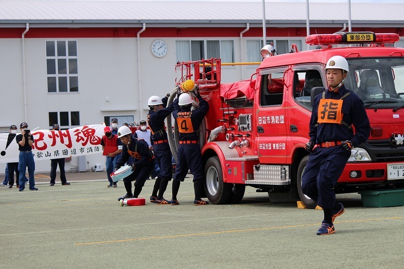運動場で制服を着た団員たちが消防車に資機材を積み込んでいる写真