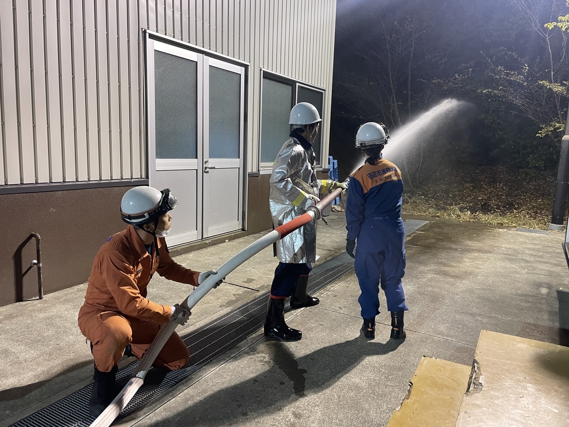 建物の外で防火服を着た作業員たちが放水訓練をしている写真
