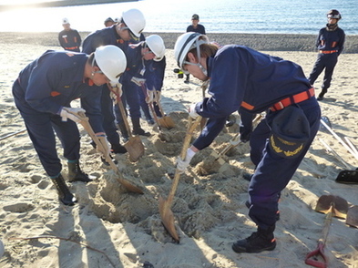 海岸で防災服を着た職員たちが協力して土のうを設置している写真