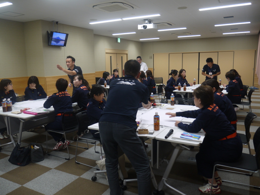 研修室で防火服を着た団員たちが資料を囲んで話し合いをしている写真