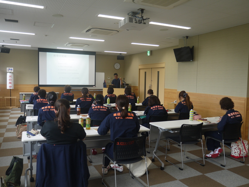 研修室で防火服を着た団員たちが机に向かって研修の講義を受けている写真