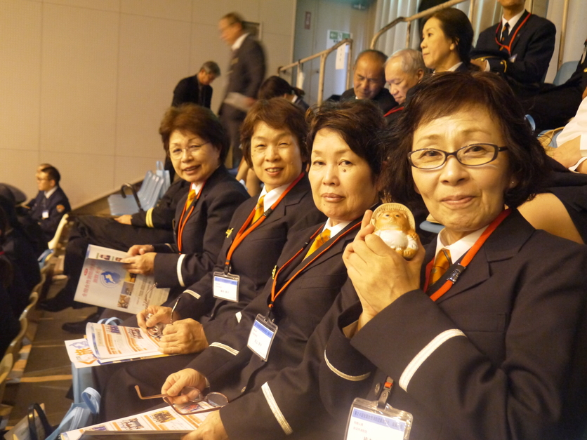 観客席で制服姿の女性消防団員たちが並んで座っている正面からの写真