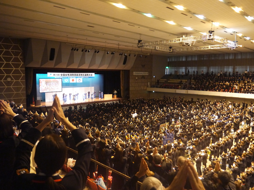 大会会場で参加者全員が拍手をしている全体の写真