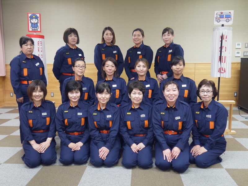 研修室で防火服を着た女性団員たちが整列して記念撮影している写真