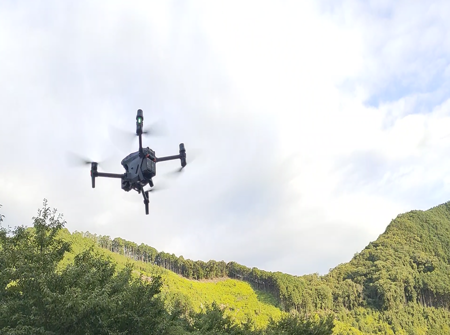 グレー色のドローンが山間の空を飛んでいる写真