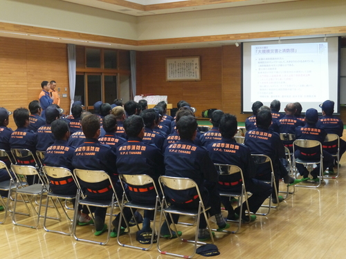 研修会場で消防団の団員たちがパイプ椅子に着席して講義を聞いている後ろ姿の写真