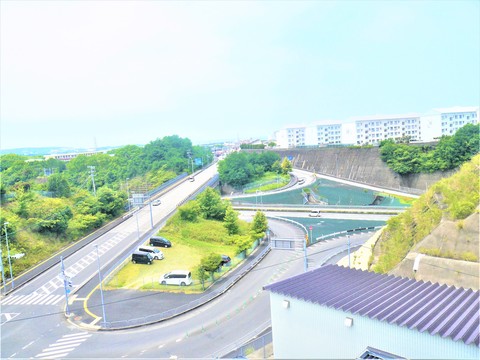高台から見下ろした道路と調整池がある街の景色を写した写真