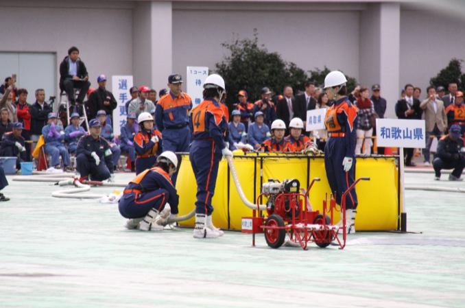 競技会場で防火服を着た女性団員たちが可搬ポンプの準備をしている写真