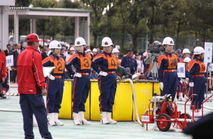 競技会場で防火服を着た女性団員たちが整列して競技開始を待っている写真