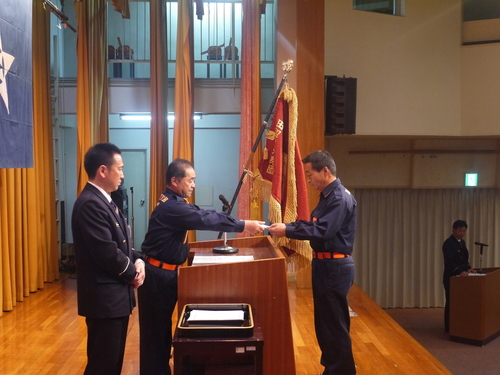 式典会場の壇上で消防団の団員が辞令を受け取っている写真