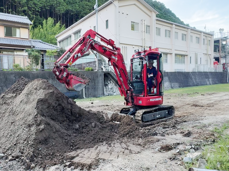防火服を着た隊員が赤いショベルカーを操作し、土砂をすくい上げている様子の写真