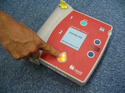 AEDのオレンジ色のボタンを押している様子のクローズアップ写真