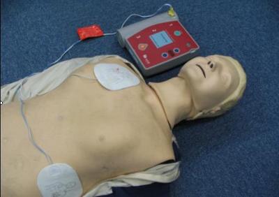 電極パッドが取り付けられて横たわっている人の横にAEDがある写真