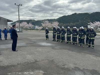 咲いている桜の木の前で消防長の訓示を聞いてる消防隊員たちの写真