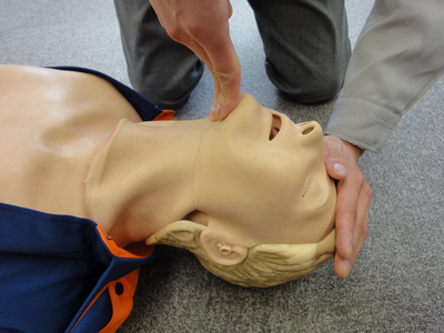 横たわっている人の顎に指をあて気道確保をする男性の写真