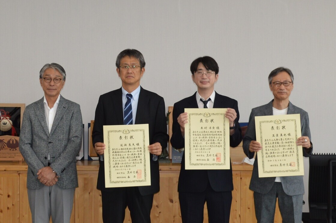 両手で表彰状を持ち横一列に並んで立っている4人の男性