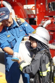 男の子がヘルメットを被り消防服を着て手にぐるぐる巻きのロープを持っている写真