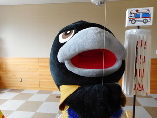 天井に設置された火災報知器の点検ひもを引く、カラスのキャラクター着ぐるみを着た人物の写真