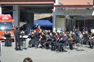 屋外で指揮をしている人と椅子に座って楽器を演奏している人たちの写真